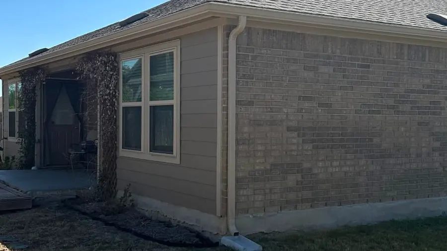 A finished PSG job: gutter along the eave of a brick and siding house, with the downspout coming down the corner to a splash block