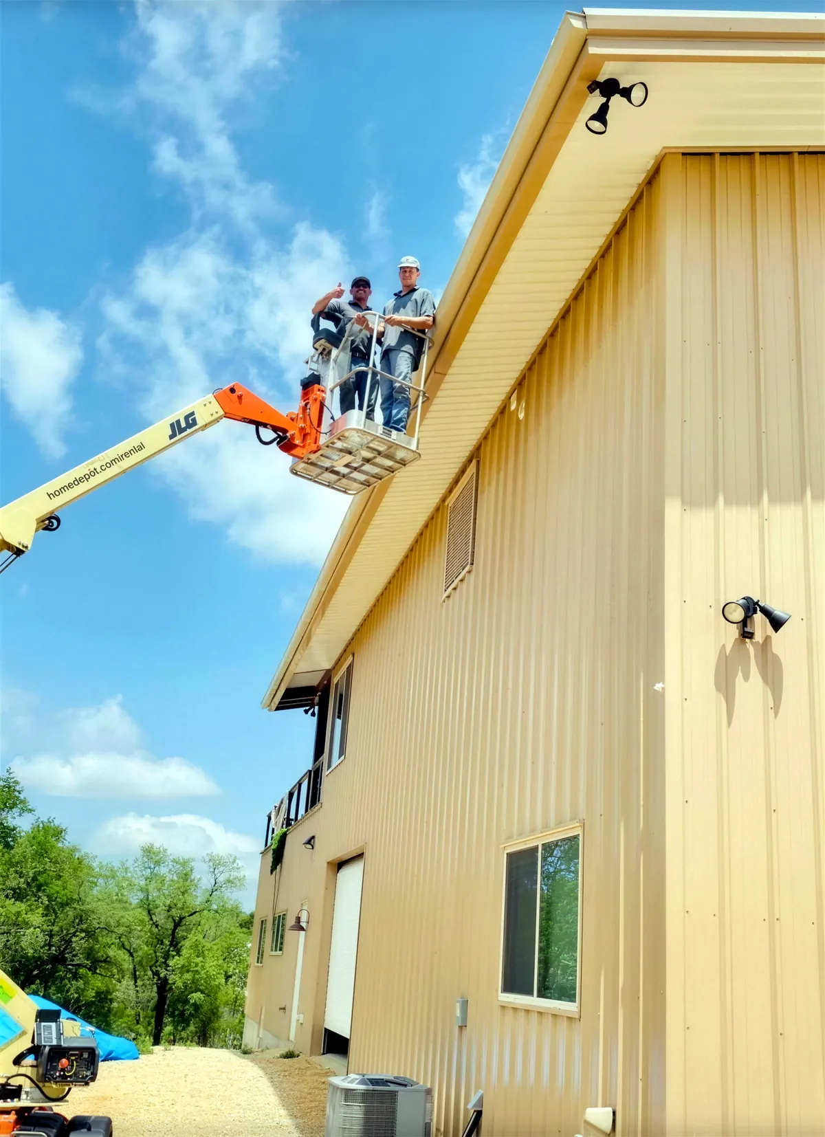 Two PSG crew members on a lift at the eave of a tan metal building, April 2023