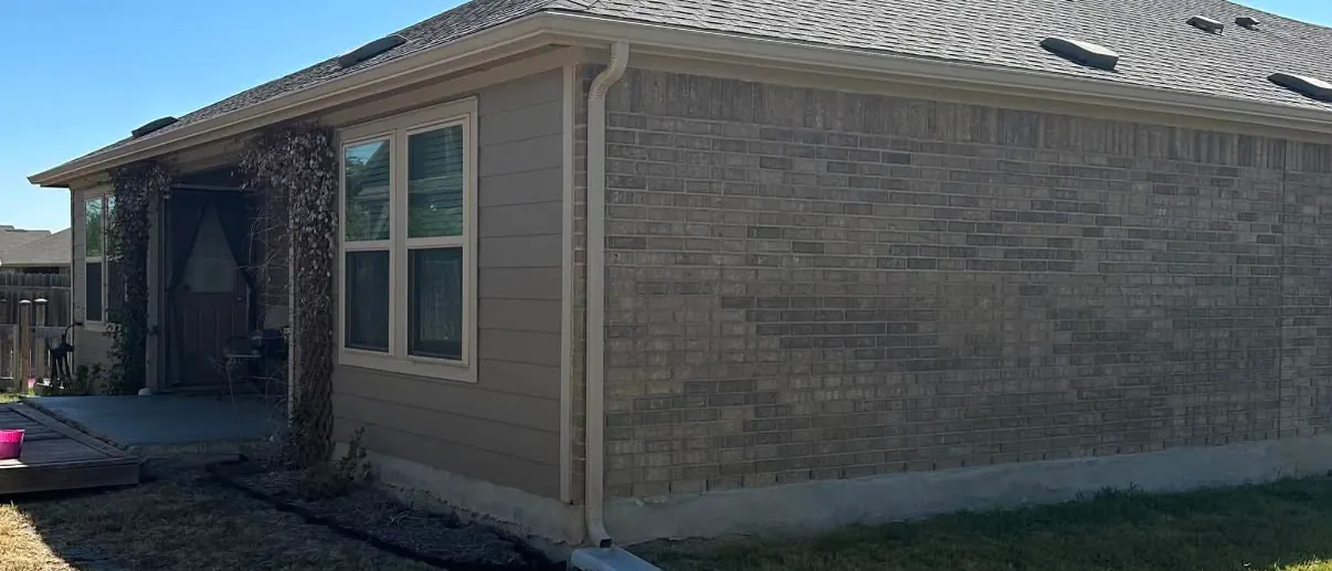 A PSG job from August 2023: new gutter along the eave of a brick and siding house, with a tan downspout at the corner