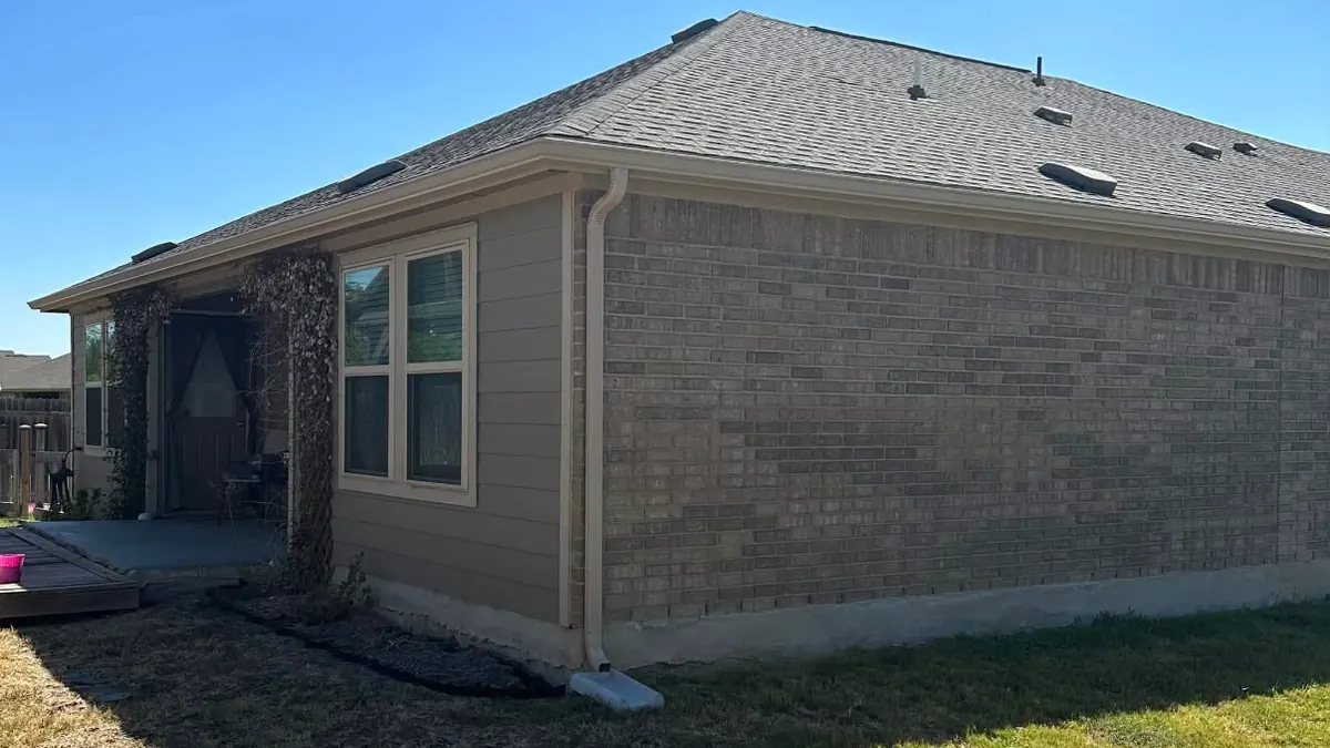 A PSG job from August 2023: a brick and siding house with a new gutter along the eave and a tan downspout at the corner emptying onto a splash block