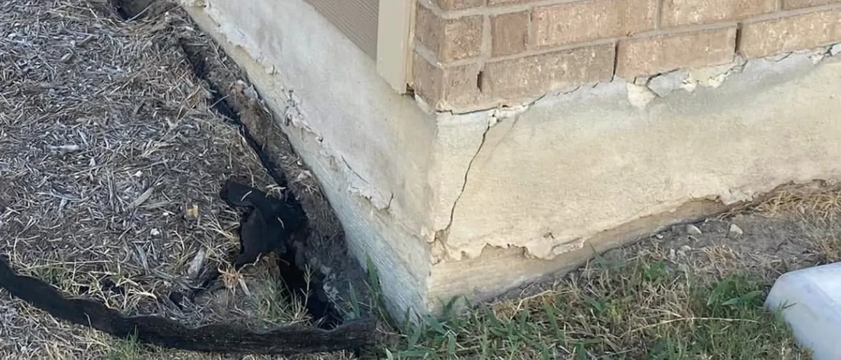 Soil and mulch washed away from the corner of a slab, leaving the concrete edge cracked and exposed